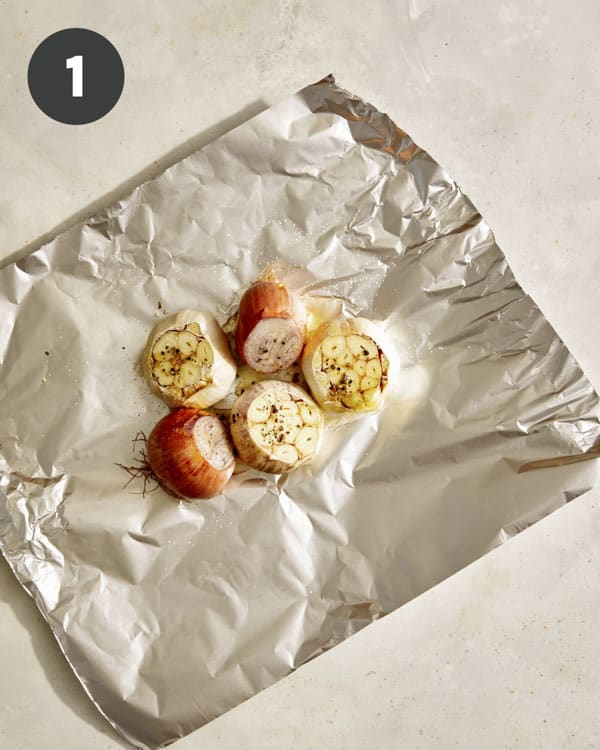 Garlic and shallots drizzled with salt and pepper on foil.