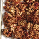 Easy crunchy homemade granola recipe on a baking sheet with a spoon.