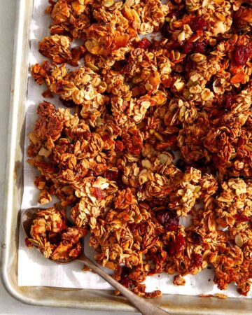 Easy crunchy homemade granola recipe on a baking sheet with a spoon.