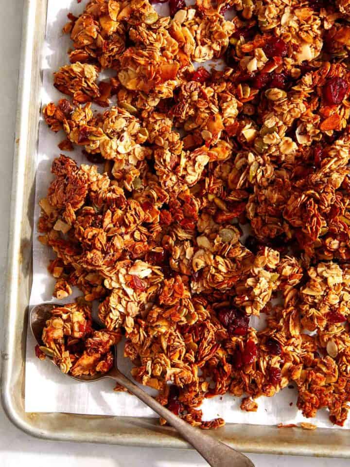 Easy crunchy homemade granola recipe on a baking sheet with a spoon.