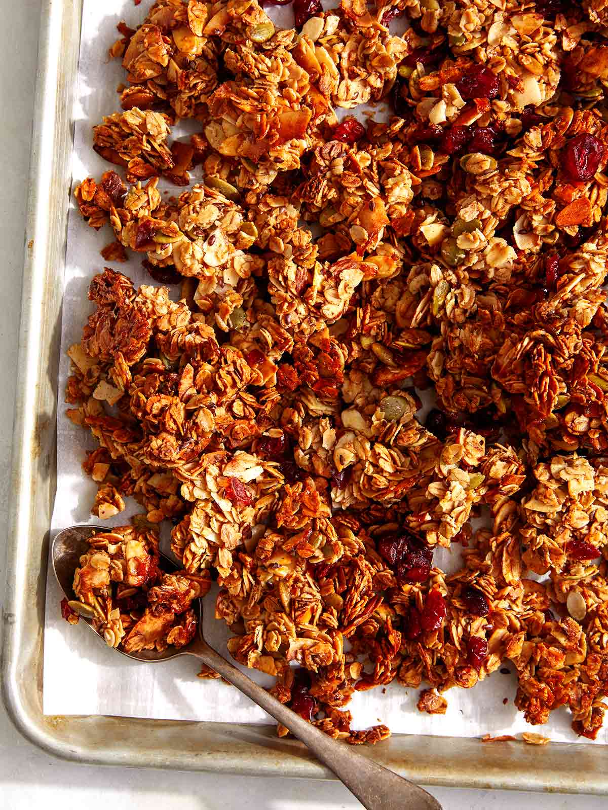 Easy crunchy homemade granola recipe on a baking sheet with a spoon. 