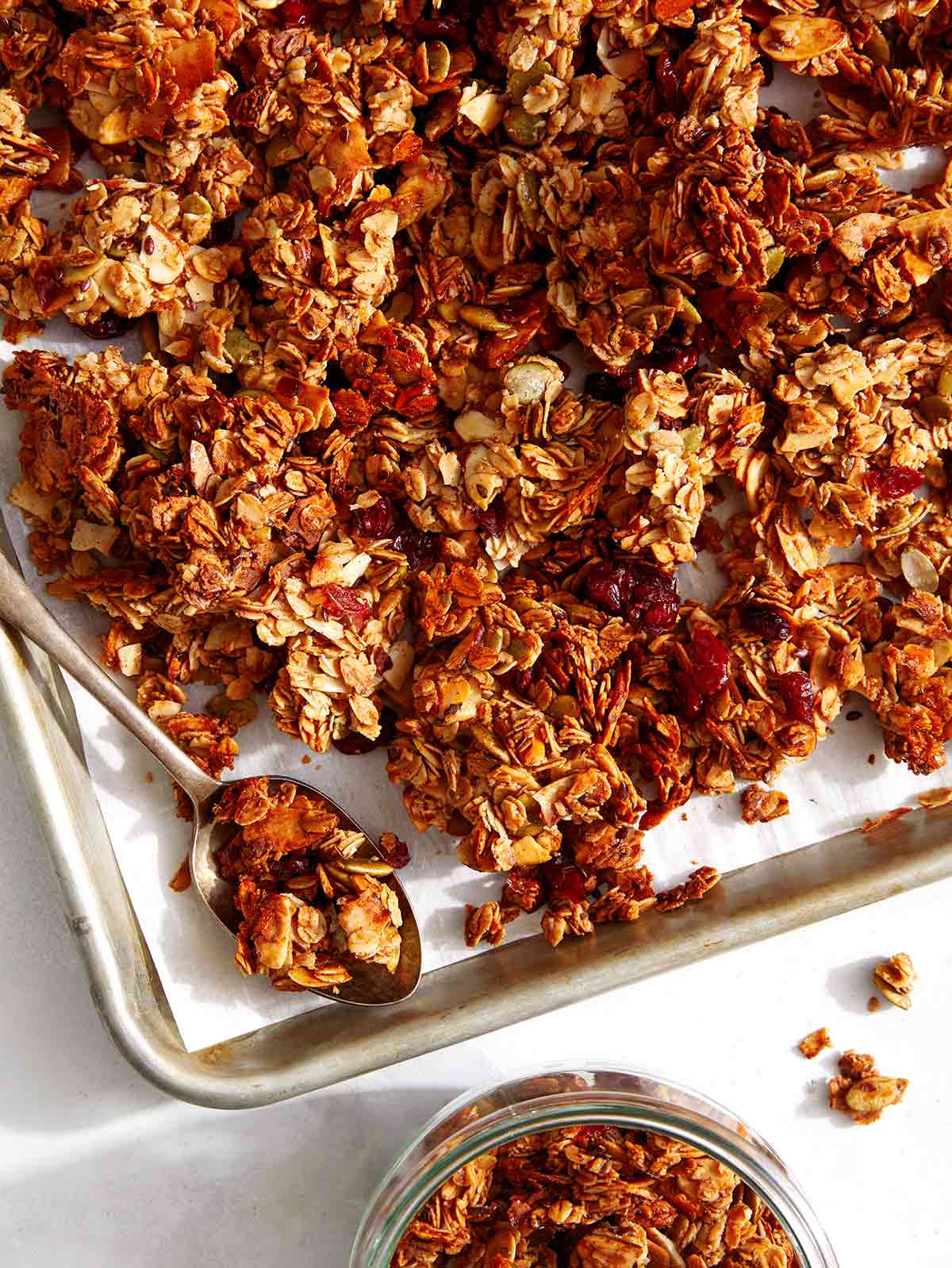 Homemade granola on a baking sheet being put into a jar. 