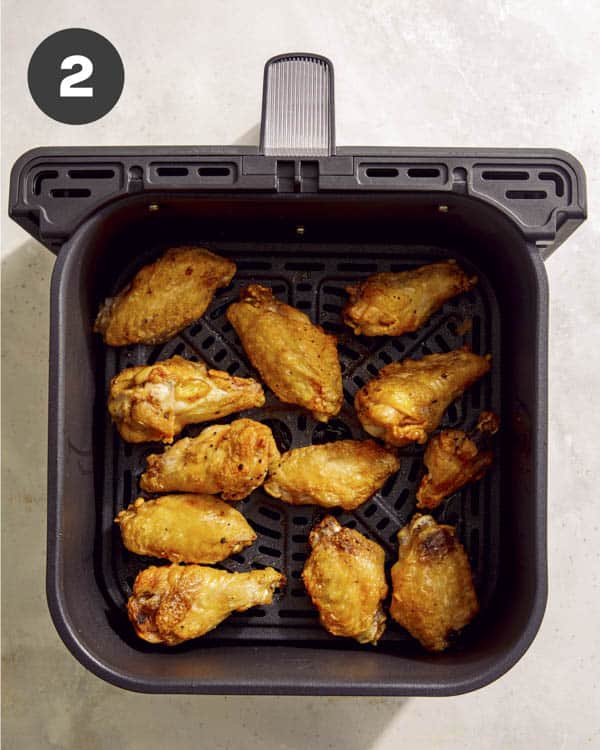 Buffalo wings in an air fryer being cooked.