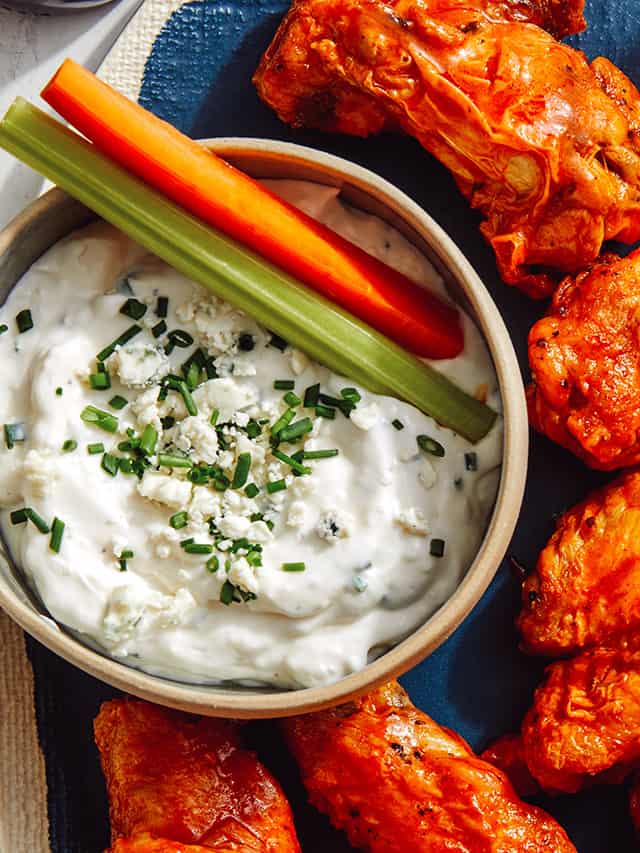 chicken wings next to blue cheese dressing in bowl with celery and carrots