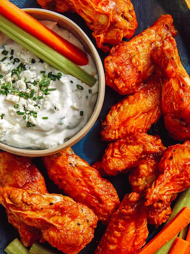 chicken wings next to blue cheese dressing in bowl with celery and carrots