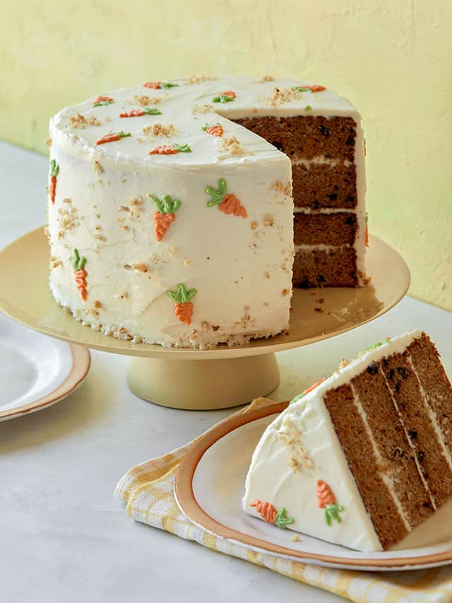 carrot cake on a cake plate sliced next to a plate with the slice of cake