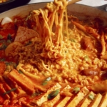 Budae Jjigae being served with chopsticks.