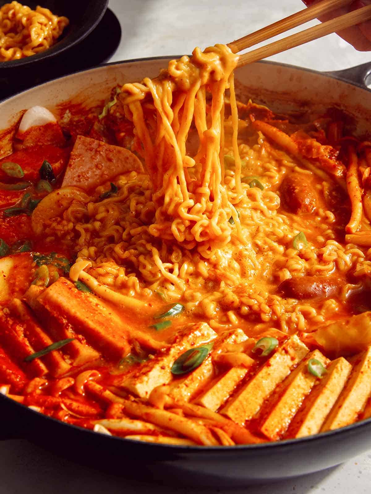 Budae Jjigae being served with chopsticks. 