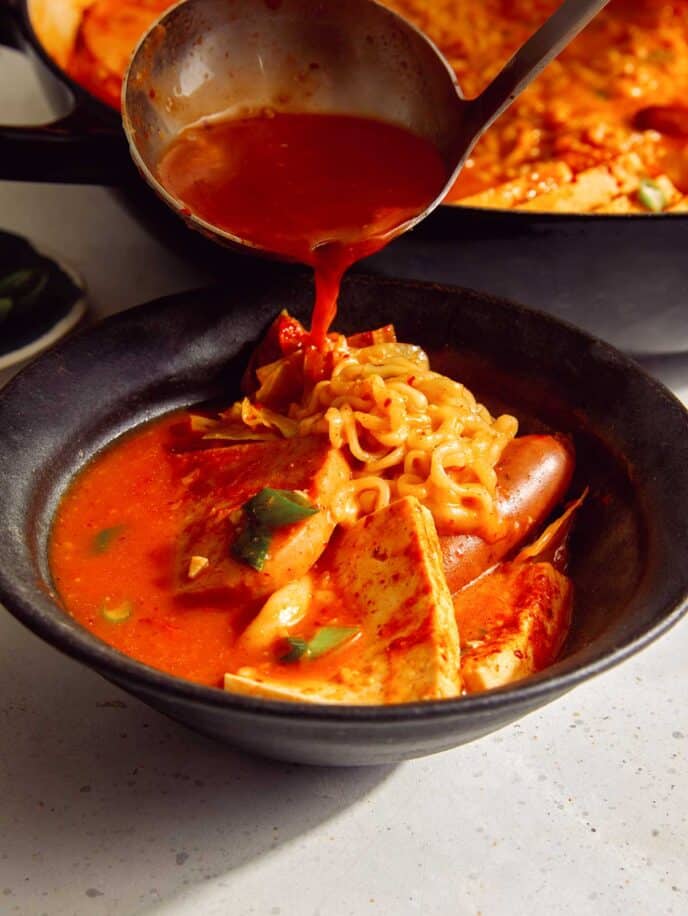 Korean army stew or Budae Jjigae being ladled into a bowl. 