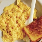 Scrambled eggs in a skillet with toast on the side.