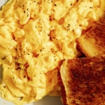 Scrambled eggs in a skillet with toast.