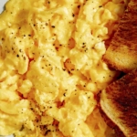 Scrambled eggs in a skillet with toast.