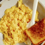 Scrambled eggs in a skillet with toast on the side.