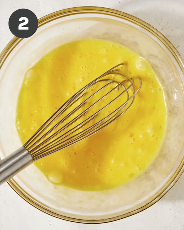 Scrambled eggs in a bowl with a whisk.