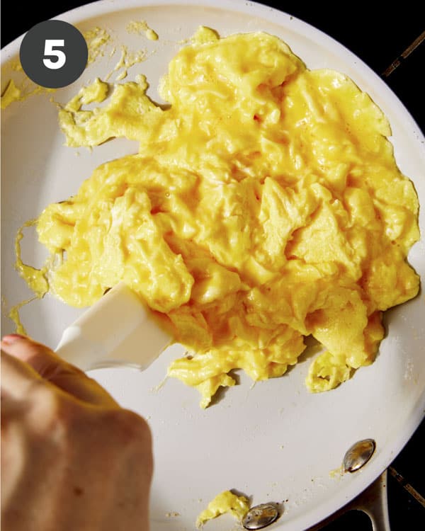 Scrambled eggs in a skillet being cooked with a rubber spatula. 