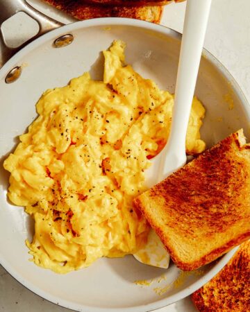 Scrambled eggs in a skillet with toast on the side.