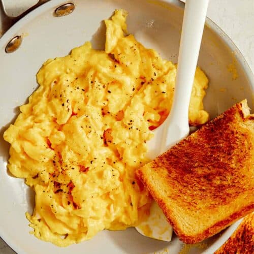 Scrambled eggs in a skillet with toast on the side.