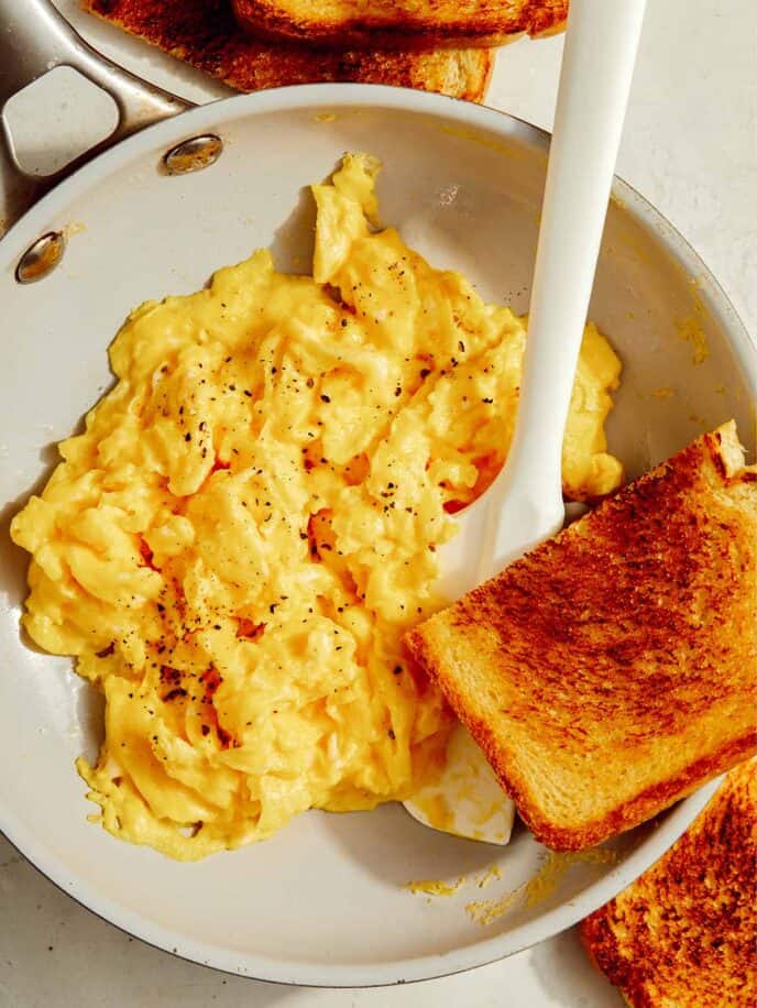 Scrambled eggs in a skillet with toast on the side.