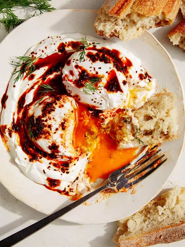 turkish eggs cilbir in a bowl with bread and a fork