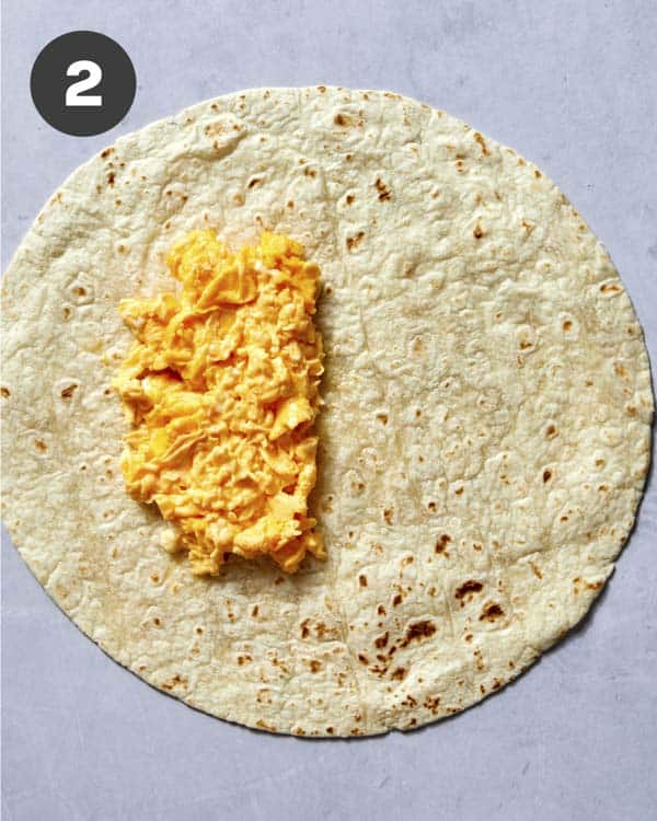Scrambled eggs on a tortilla to make a breakfast burrito.