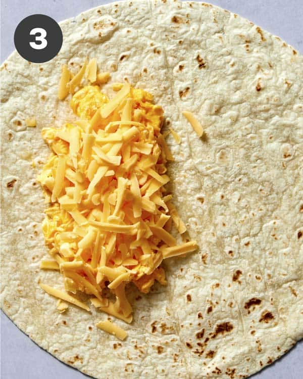 Adding cheese to a breakfast burrito. 