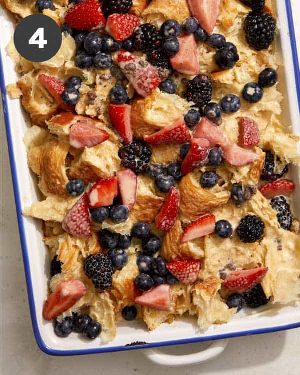 Croissants and berries in a baking dish with an egg mixture poured over the top. 