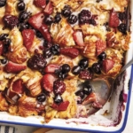 Triple berry bread pudding in a baking dish with a scoop out.