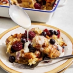 Bread pudding on a plate with glaze being spooned on.