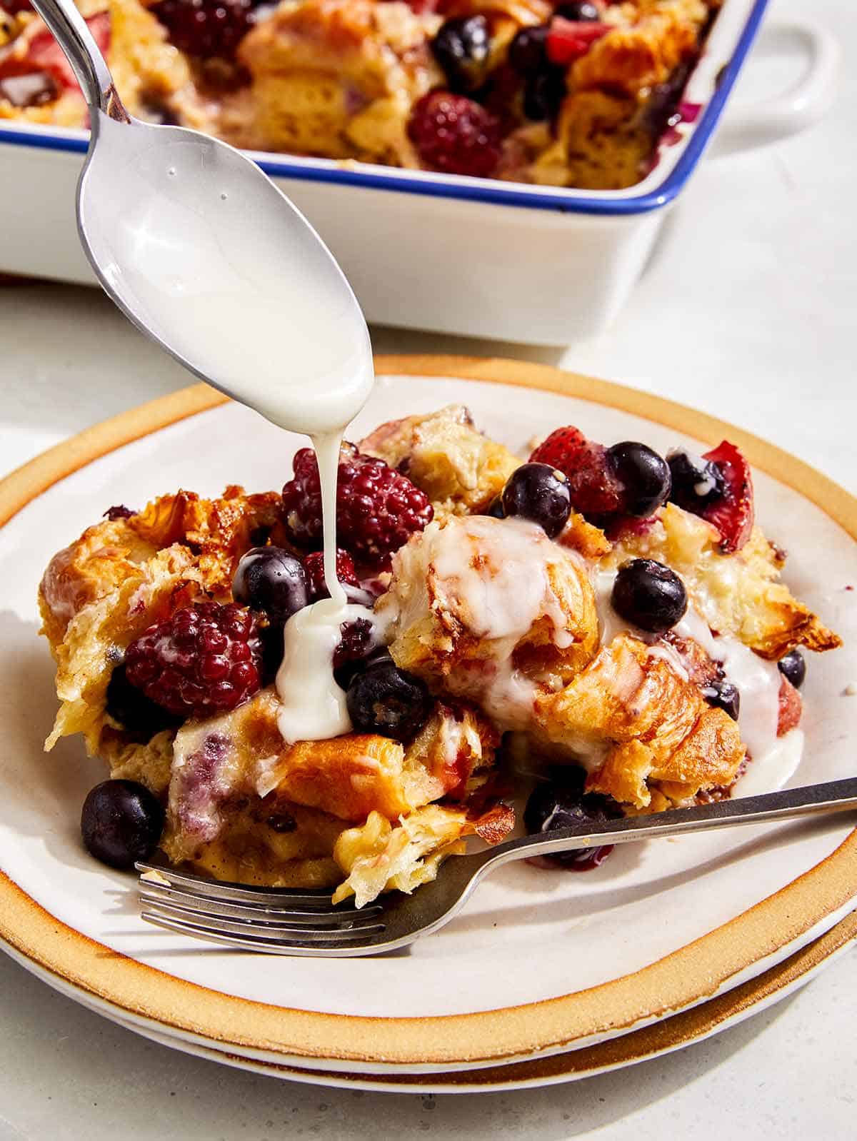 Berry bread pudding with a glaze being spooned on top.