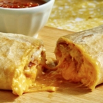A cheesy breakfast burrito cut in half with salsa on the side.