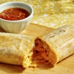 A cheesy breakfast burrito cut in half with salsa on the side.