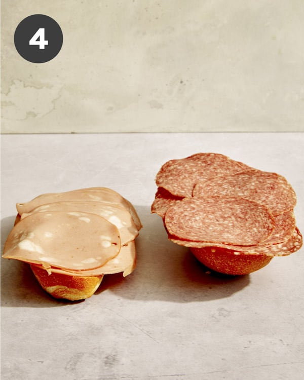Grinder sandwich assembly with meat being placed on bread.