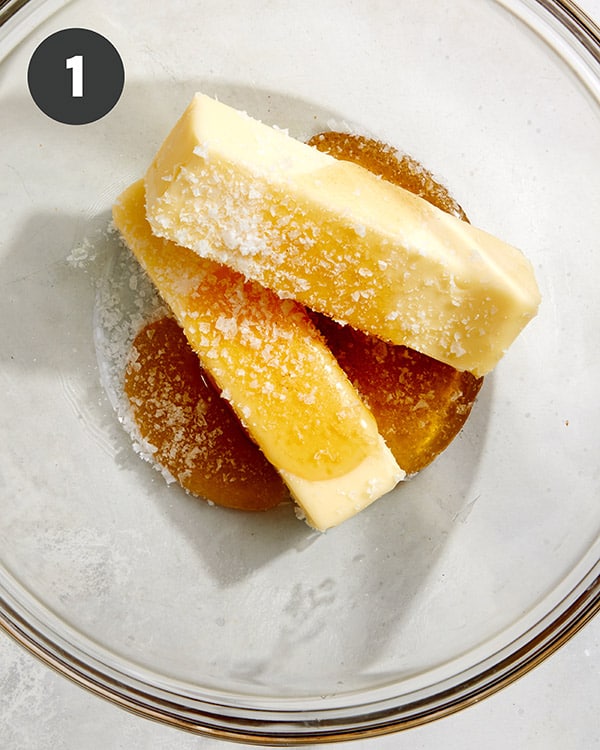 Softened sticks of butter, honey, and salt in a glass bowl. 