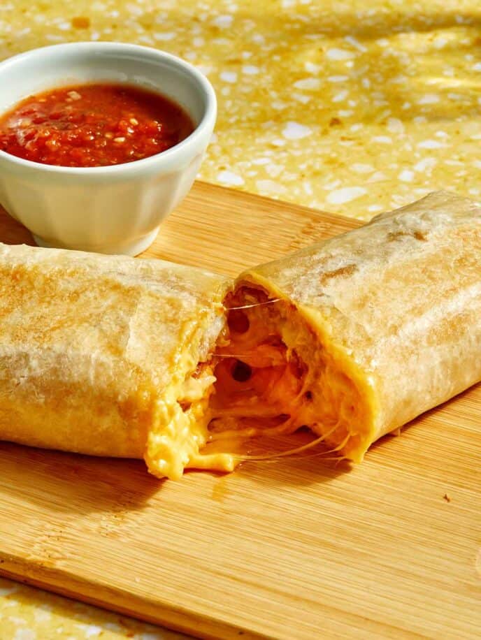 A cheesy breakfast burrito cut in half with salsa on the side.