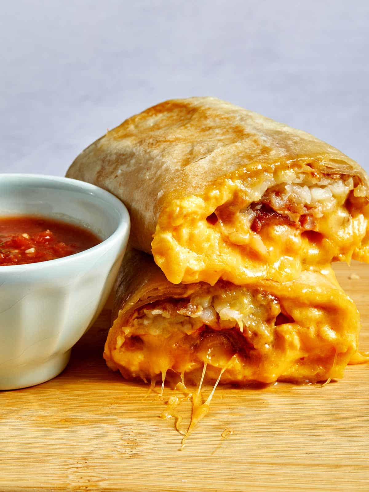A breakfast burrito cut in half with cheese oozing out. 