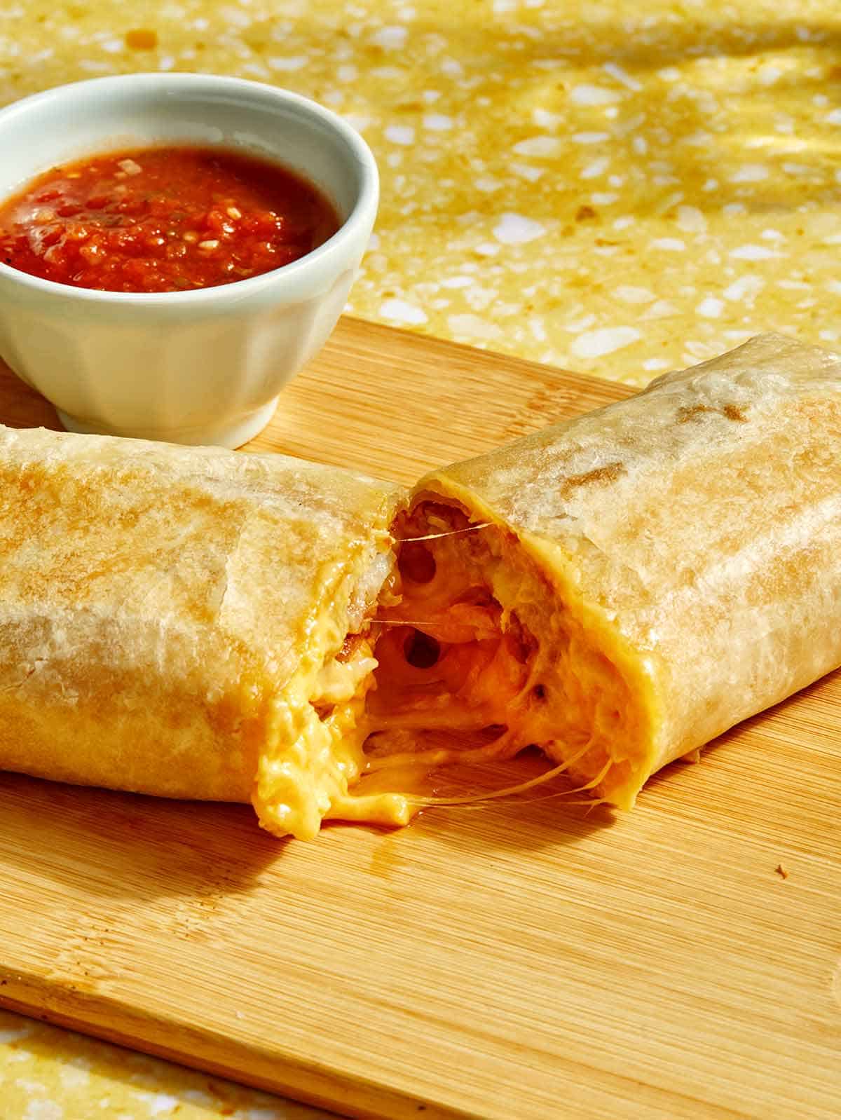 A cheesy breakfast burrito cut in half with salsa on the side. 