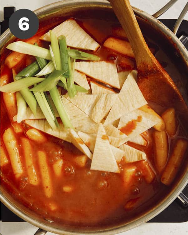 Tteokbokki recipe with fish cakes and green onion added in a pot.