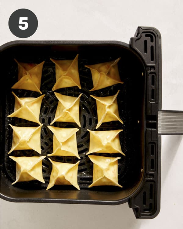 Crab rangoon in an air fryer basket.