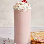 A strawberry milkshake in a glass with a cherry on top.