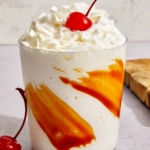 Caramel milkshake in a glass with whipped cream and a cherry.
