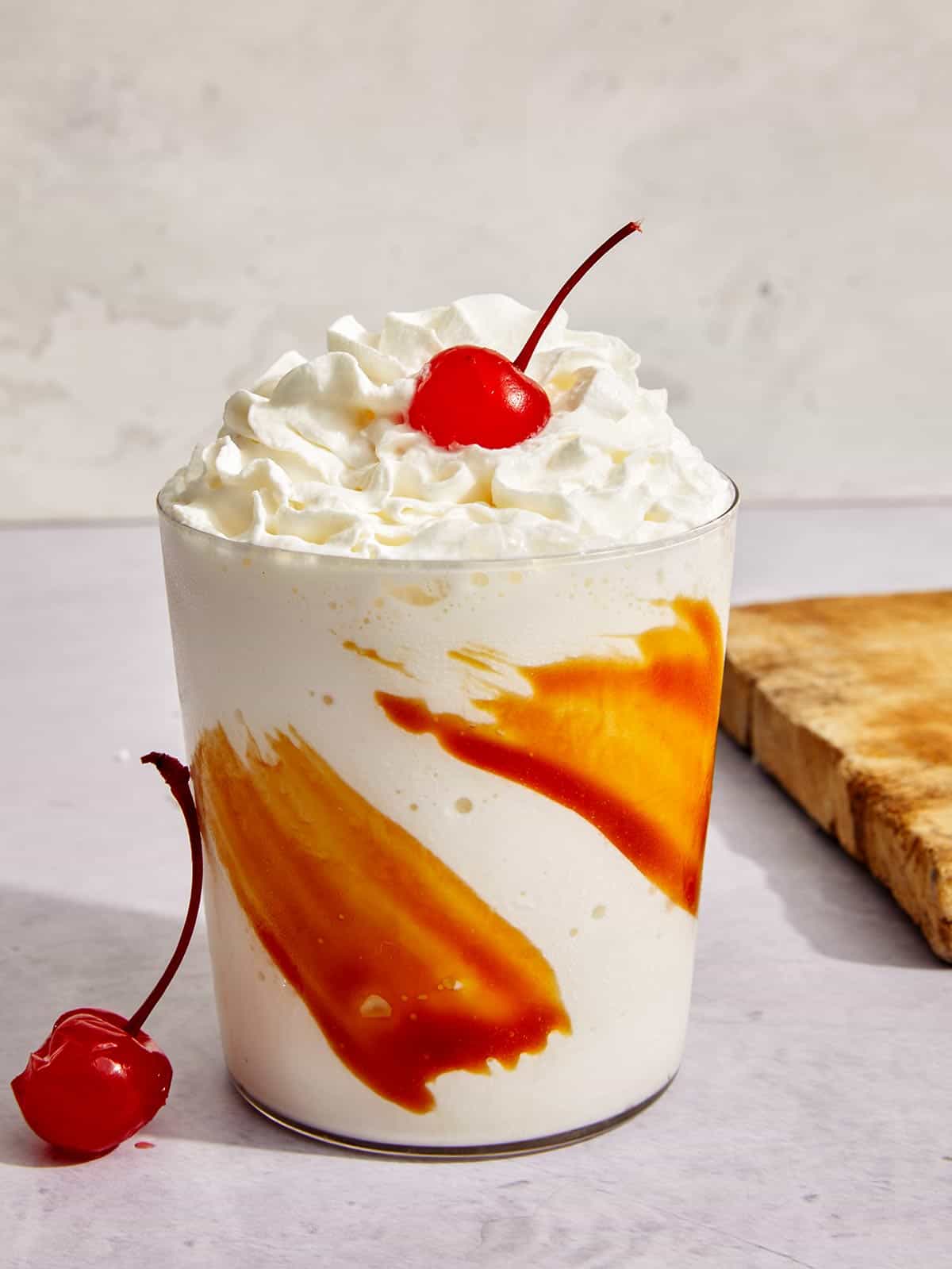 Caramel milkshake in a glass with whipped cream and a cherry.