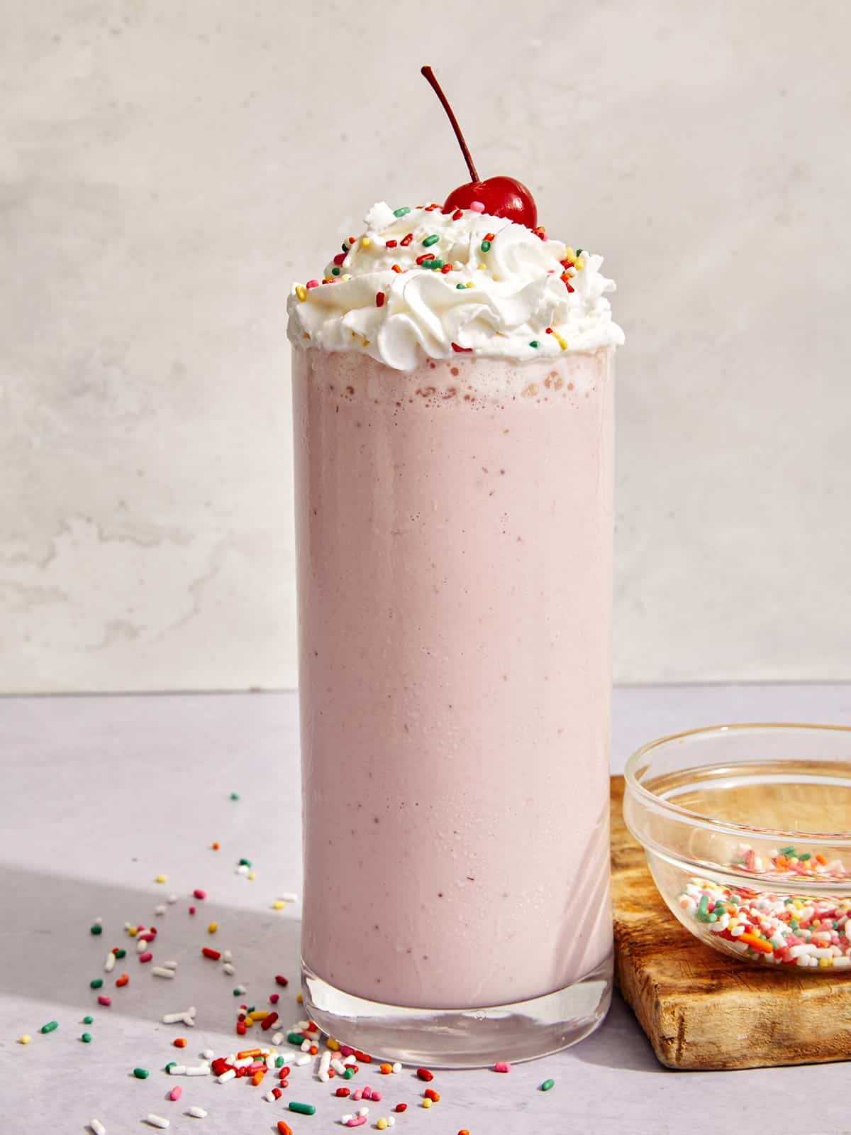 A strawberry milkshake in a glass with a cherry on top.