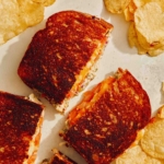 Tuna melt cut in half on a kitchen counter with potato chips.