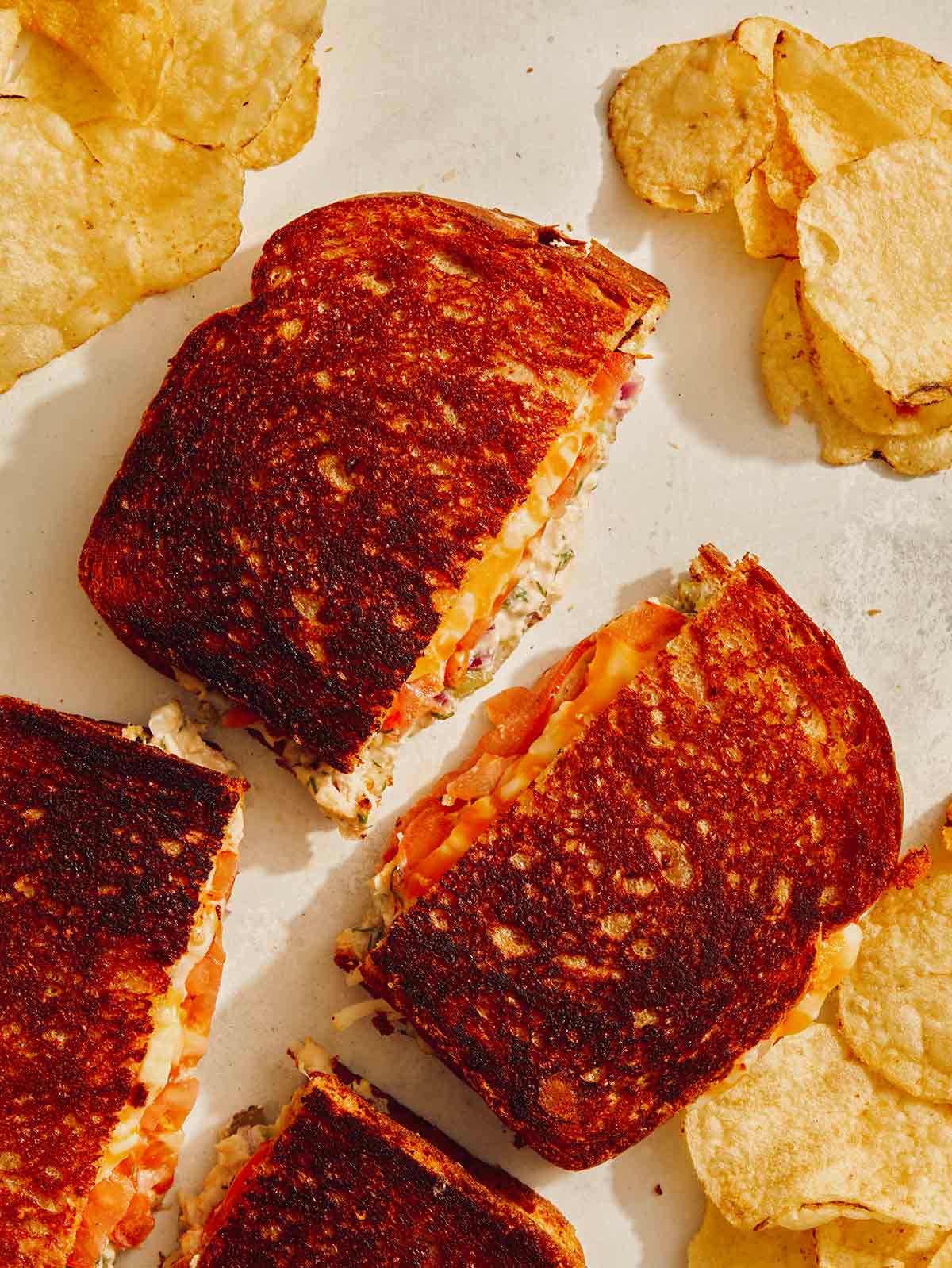 Tuna melt cut in half on a kitchen counter with potato chips.