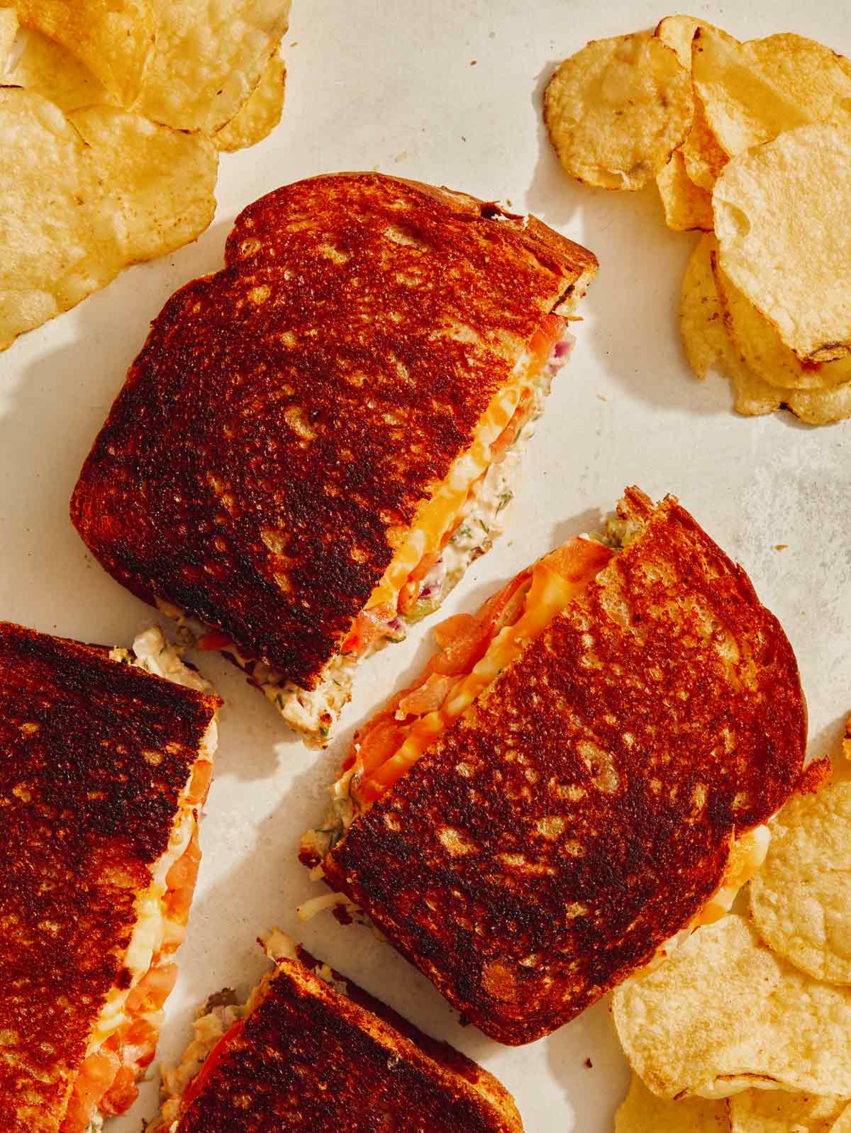 Tuna melt cut in half on a kitchen counter with potato chips. 