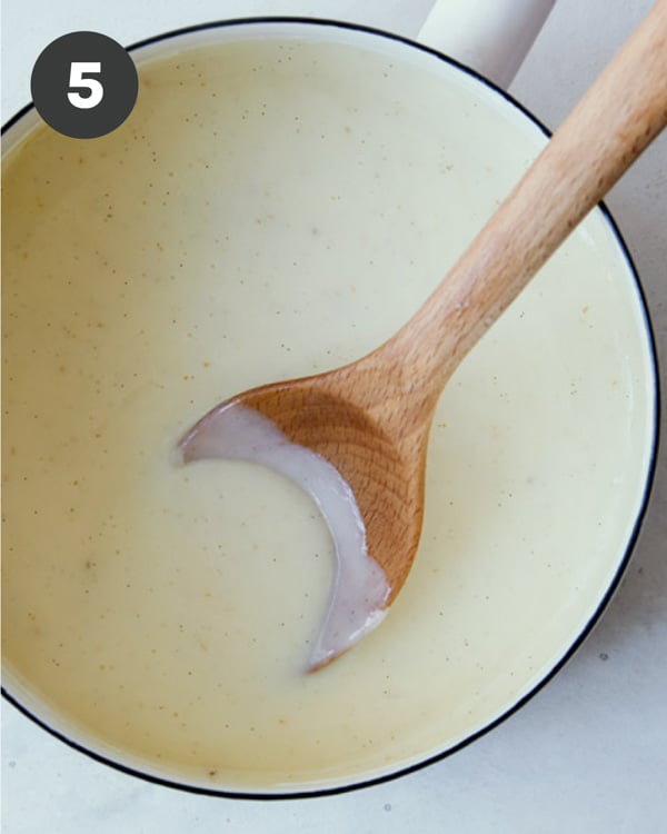 Banana pudding being made in a pot with a wooden spoon. 