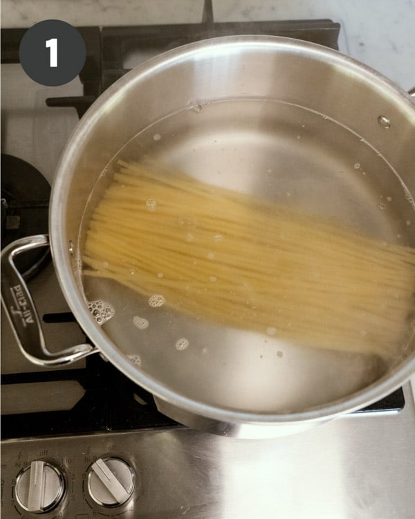 Uncooked bucatini noodles in a pot of water on stovetop.