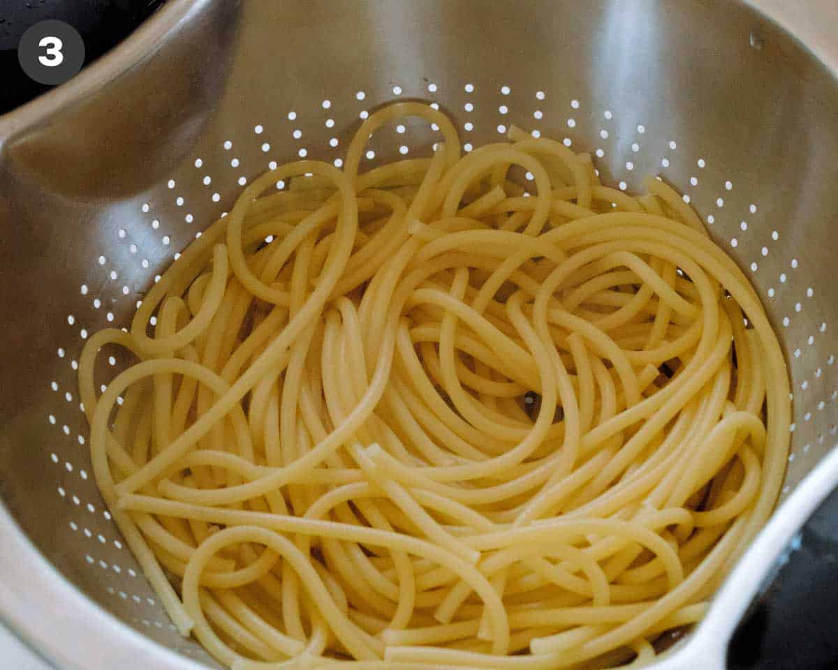 Cooked bucatini noodles in a strainer.