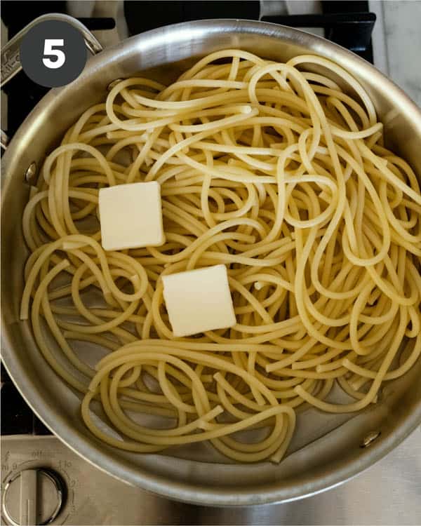 Cooked bucatini noodles in a skillet with pads of butter.