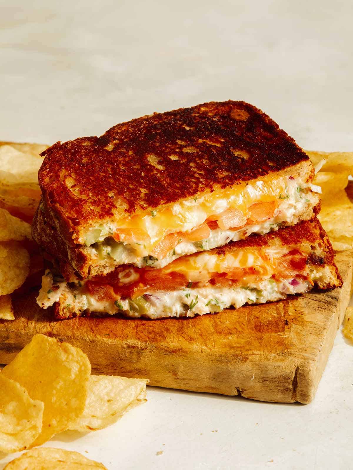 Tuna melt sandwich on a cutting board with potato chips. 